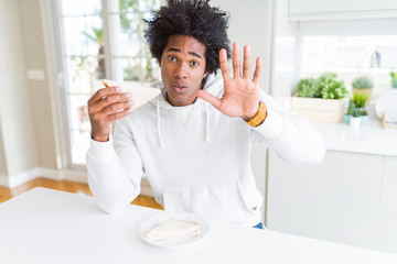 Fototapeta na wymiar African American man eating handmade sandwich at home with open hand doing stop sign with serious and confident expression, defense gesture