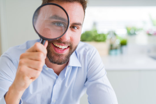 Handsome business man holding magnifying glass close to face, big eyes and funny expression