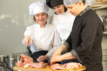 Chef teaches trainee a group of people to cut a chicken. Master Class on the background of the kitchen.