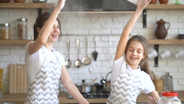 Two sisters having fun at the kitchen. Giving five with hands in flour. Making flour clooud. Joy, fun.