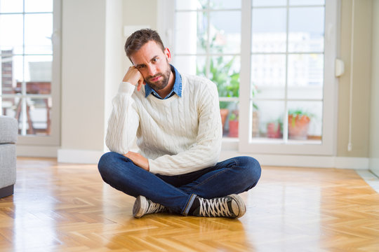 Handsome man wearing casual sweater sitting on the floor at home thinking looking tired and bored with depression problems with crossed arms.