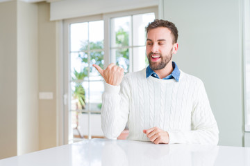 Handsome man wearing casual sweater smiling with happy face looking and pointing to the side with thumb up.