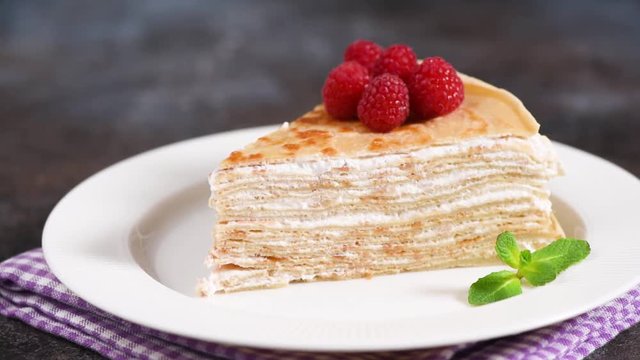 Crepe cake with pastry cream on white plate decorated with raspberries and mint leaf