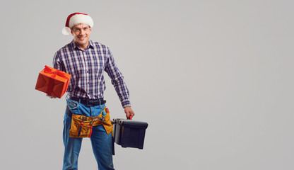 Repairman in Santa hat with a gift on a gray background.