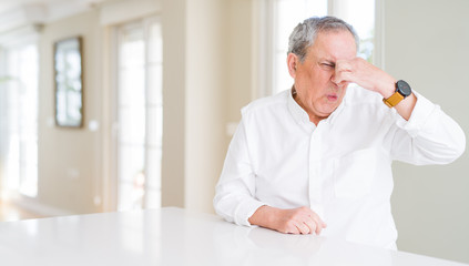 Handsome senior man at home smelling something stinky and disgusting, intolerable smell, holding breath with fingers on nose. Bad smells concept.