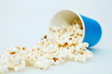 Hot fresh popcorn poured out of blue paper cup on a white background