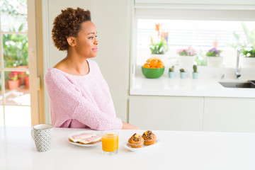 Obraz na płótnie Canvas Young african american woman eating breaksfast in the morning at home looking to side, relax profile pose with natural face with confident smile.