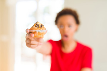 Young african american woman eating chocolate chips muffins scared in shock with a surprise face, afraid and excited with fear expression