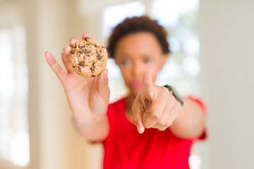 Young african american woman eating chocolate chips cookies pointing with finger to the camera and to you, hand sign, positive and confident gesture from the front