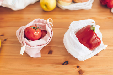 Fresh groceries in reusable eco bags and vegetables in plastic polyethylene bag on wooden table....