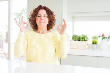 Beautiful senior woman wearing yellow sweater relax and smiling with eyes closed doing meditation gesture with fingers. Yoga concept.