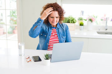 Senior woman working using computer laptop stressed with hand on head, shocked with shame and...