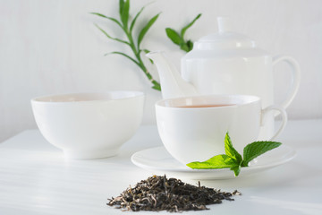 Still life cup of green tea with green tea dry leaves on white. Teatime.