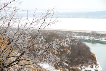 Winter landscape, branches of bushes and trees are covered with white frost on a cliff, a wide river