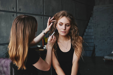 Fototapeta premium The girl is sitting on a chair. girl makes makeup stylist tassel.