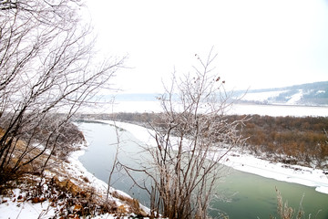 Winter landscape, the bed of a wide river, the shore in the snow and bushes, branches in the trees in the other, view from the top