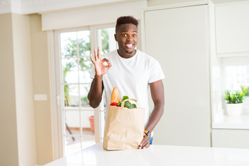African american man holding paper bag full of fresh groceries doing ok sign with fingers, excellent symbol