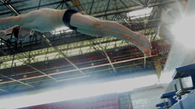 Muscular swimmer jumping from starting block in a swimming pool