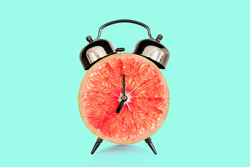 Grapefruit slice on alarm clock, blue pastel background. fruit and vitamins diet at breakfast nutrition concept