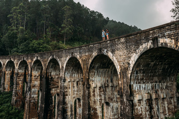 Obraz premium Loving couple on the edge of the bridge. Man and woman traveling around Asia. The couple travels to Sri Lanka. Man and woman in an unusual place. Nine-arch bridge. Travellers in Asia. Hold hands