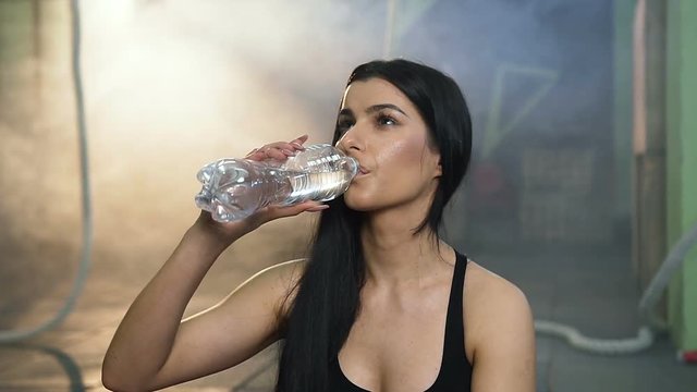 Portrait shot of attractive fit woman drinking water after training in the gym.