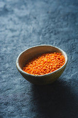 Red lentils in a bowl close up on dark stone background