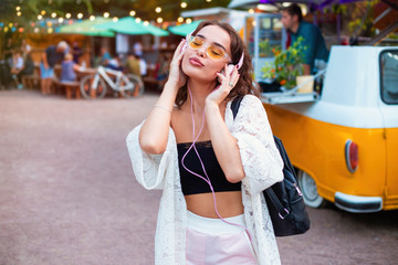 Fototapeta premium Half length of young beautiful caucasian curly hair woman listening music with headphones, looking downward smiling - music, technology, relaxing concept 