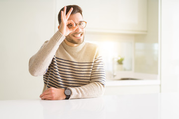 Young handsome man wearing glasses at home with happy face smiling doing ok sign with hand on eye looking through fingers