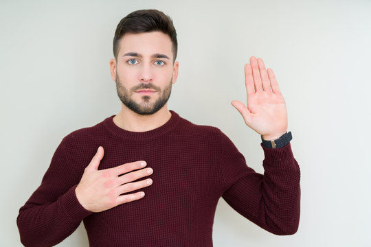 Young handsome man wearing a sweater over isolated background Swearing with hand on chest and open palm, making a loyalty promise oath