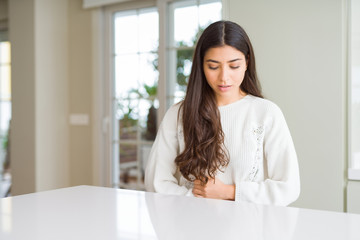 Young beautiful woman at home on white table with hand on stomach because nausea, painful disease feeling unwell. Ache concept.