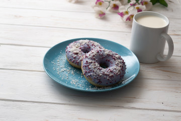 Donuts on a blue plate with a cup of milk on a white wooden background
