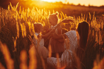 happy family, mom and two daughters. Mother plays with her daughter on the street in the park at sunset.