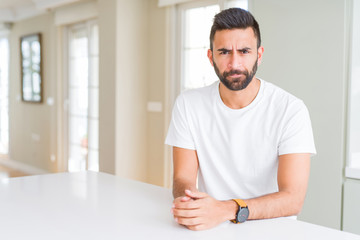 Handsome hispanic man casual white t-shirt at home skeptic and nervous, frowning upset because of problem. Negative person.
