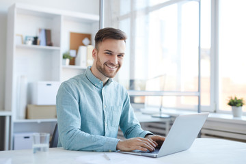 Portrait of handsome young man working in office and smiling happily at camera, copy space