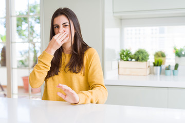 Beautiful young woman wearing yellow sweater smelling something stinky and disgusting, intolerable smell, holding breath with fingers on nose. Bad smells concept.