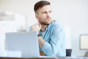 Portrait of handsome businessman looking away pensively while sitting at workplace in office, copy space
