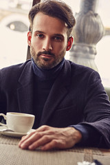 Thinking handsome man sitting in cafe and drinking cup of coffee on the breakfast. Closeup