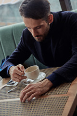 Thinking handsome bearded man sitting in cafe and drinking cup of coffee on the breakfast. Closeup