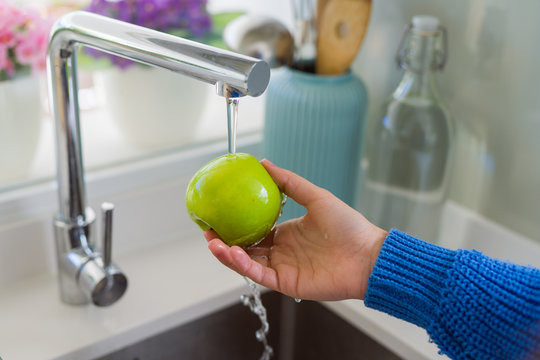 Young woman washing vegetables and fruit using water from sink