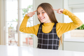 Young beautiful blonde kid girl wearing casual yellow sweater at home smiling pointing to head with both hands finger, great idea or thought, good memory