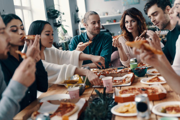 Sharing great meal. Group of young people in casual wear eating pizza and smiling while having a dinner party indoors