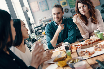 Just relaxing. Group of young people in casual wear talking and smiling while having a dinner party indoors