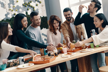 Life is better with friends. Group of young people in casual wear eating pizza and smiling while having a dinner party indoors
