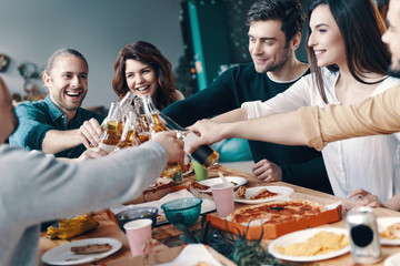 Young and carefree. Group of young people in casual wear toasting each other and smiling while having a dinner party indoors