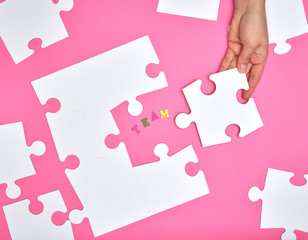 female hand puts white big puzzles on a pink background