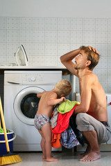 Young exhausted husband father sitting near the washing machine with pile of clothes in full...