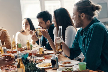 Great time with friends. Group of young people in casual wear eating pizza and smiling while having a dinner party indoors
