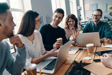 Obraz premium Inspired to work together. Group of young modern people in smart casual wear discussing something and smiling while working in the creative office