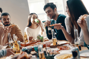 Just relaxing. Group of young people in casual wear eating pizza and smiling while having a dinner party indoors