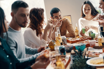 So tasty! Group of young people in casual wear eating pizza while having a dinner party indoors
